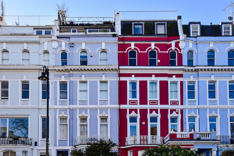 A row of elegant Victorian terraced houses in Paddington with ornate white facades, large sash windows, and decorative architectural details. The buildings feature balconies with balustrades and are i